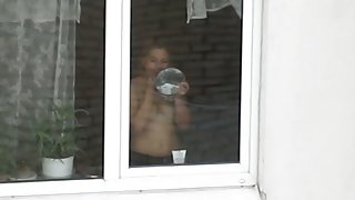 A hot topless chick puts on her makeup by a window