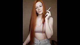 A red-haired girl with long hair smokes a cigarette with a brown filter.