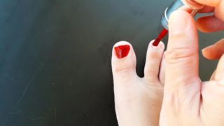 Red nail polish on toes. lady paints her toenails with red polish Regina Noir.